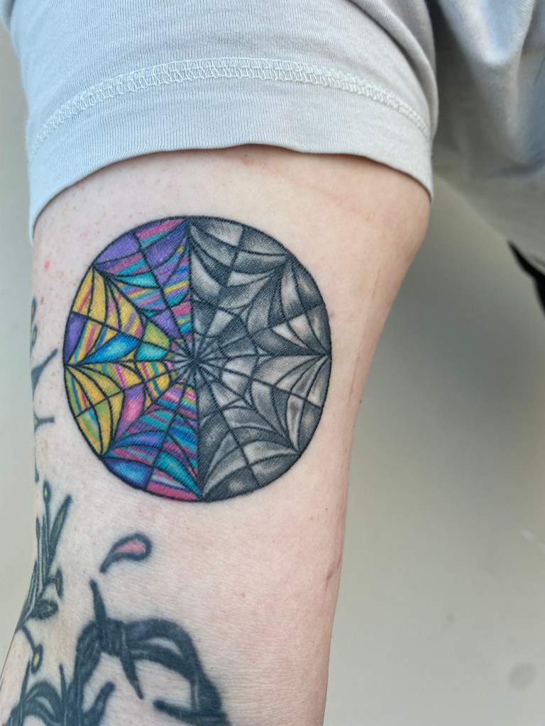 Decorative image to show artists tattoo work. Photograph of a freshly done tattoo  on an inner bicep. Tattoo is of a half colorful half desturated spiderweb. 